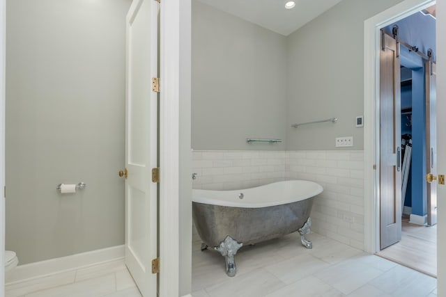 full bath featuring wainscoting, toilet, a freestanding tub, and tile walls