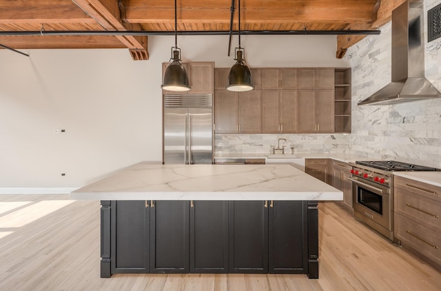 kitchen featuring wall chimney range hood, a sink, premium appliances, light wood-style floors, and a kitchen island