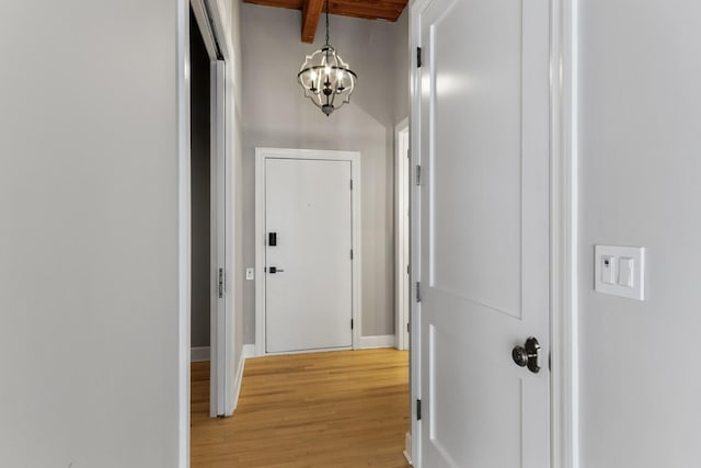 corridor featuring a chandelier, light wood-type flooring, beam ceiling, and baseboards