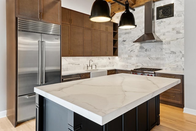kitchen featuring built in fridge, a sink, tasteful backsplash, and wall chimney range hood