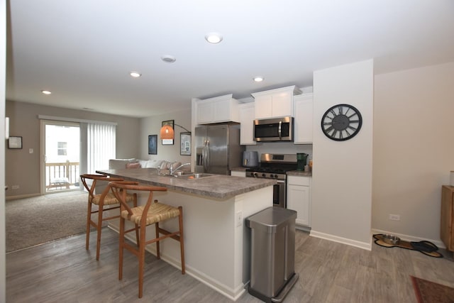 kitchen with a kitchen island with sink, a sink, white cabinetry, appliances with stainless steel finishes, and a breakfast bar area