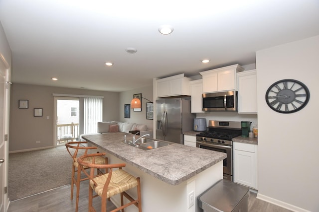 kitchen featuring a breakfast bar, wood finished floors, a sink, appliances with stainless steel finishes, and open floor plan