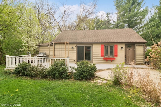 view of front of house with a shingled roof, a front lawn, and a wooden deck