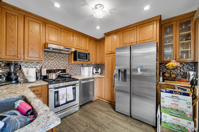791 Overland Ct, Roselle, IL 60172 - kitchen with brown cabinetry, appliances with stainless steel finishes, tasteful backsplash, light stone countertops, and under cabinet range hood