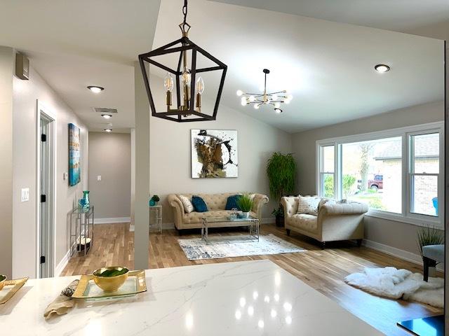 living room with light wood finished floors, vaulted ceiling, baseboards, and a chandelier