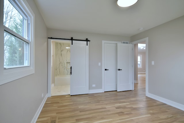 unfurnished bedroom featuring light wood-style floors, ensuite bathroom, visible vents, a barn door, and baseboards