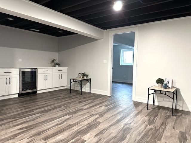 bar featuring dark wood finished floors, beverage cooler, a dry bar, and baseboards