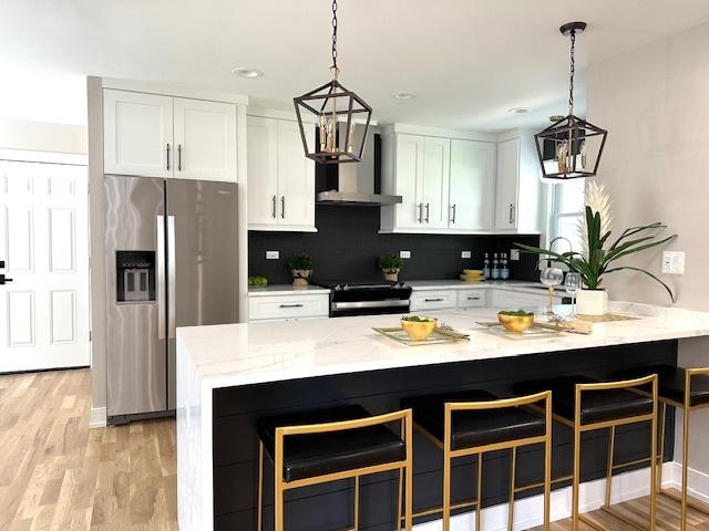 kitchen featuring wall chimney exhaust hood, backsplash, stainless steel refrigerator with ice dispenser, white cabinetry, and stove