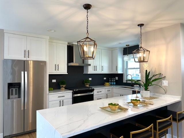 kitchen featuring wall chimney range hood, a kitchen breakfast bar, a sink, electric range, and stainless steel refrigerator with ice dispenser