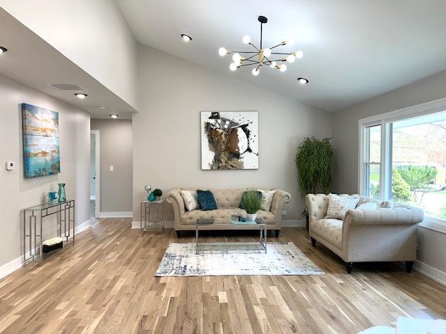 living area with light wood finished floors, baseboards, an inviting chandelier, and lofted ceiling