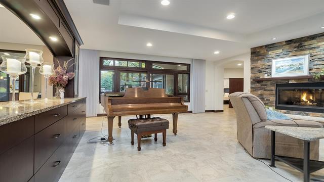 living area featuring a raised ceiling, marble finish floor, a stone fireplace, and recessed lighting