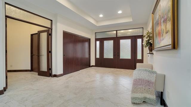 entryway with recessed lighting, a tray ceiling, baseboards, and french doors