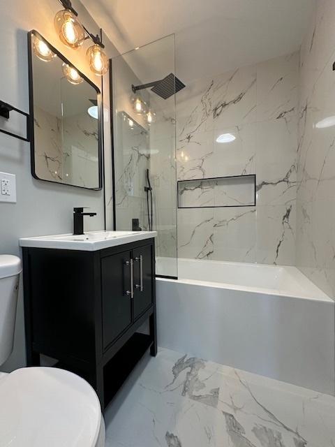 bathroom with marble finish floor, toilet, vanity, and tub / shower combination