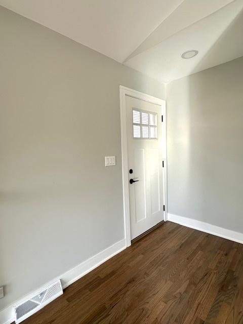 doorway featuring vaulted ceiling, baseboards, dark wood-type flooring, and visible vents