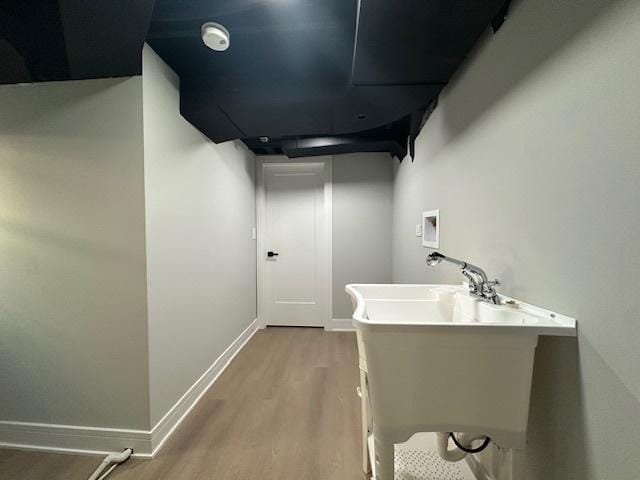 corridor with wood finished floors, baseboards, and a sink