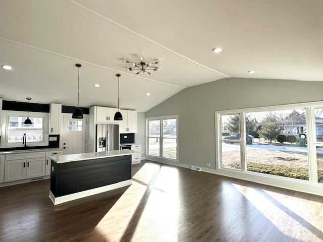 kitchen with vaulted ceiling, a center island, stainless steel fridge, decorative light fixtures, and dark wood finished floors