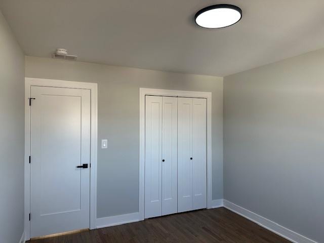 unfurnished bedroom featuring baseboards, dark wood-style floors, and a closet