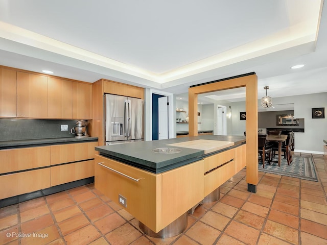 kitchen with dark countertops, a tray ceiling, stainless steel fridge, and light brown cabinetry