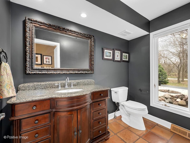 half bathroom with baseboards, visible vents, vanity, and toilet