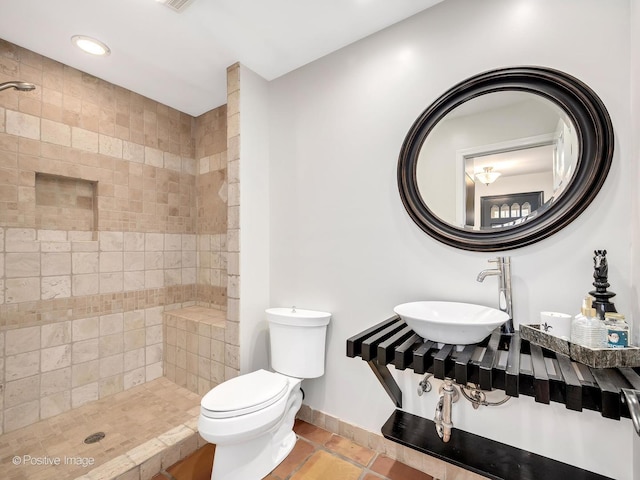 full bathroom with tile patterned flooring, toilet, tiled shower, and a sink