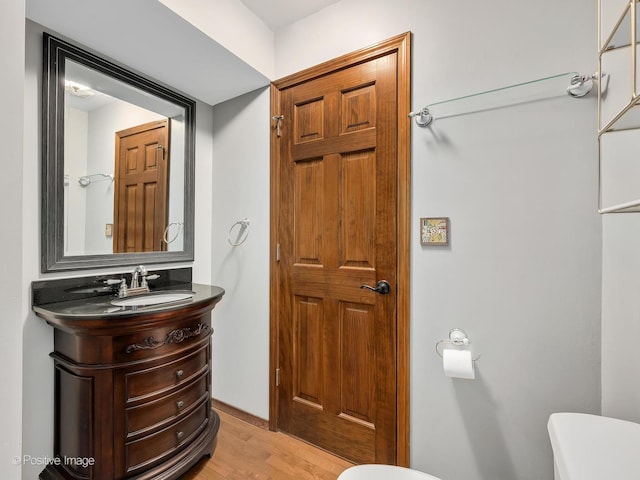 half bathroom featuring wood finished floors, toilet, and vanity