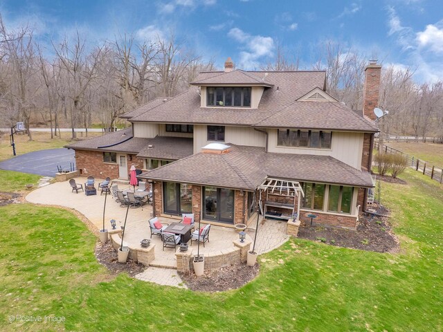 rear view of property with a yard, a patio area, a shingled roof, and a chimney