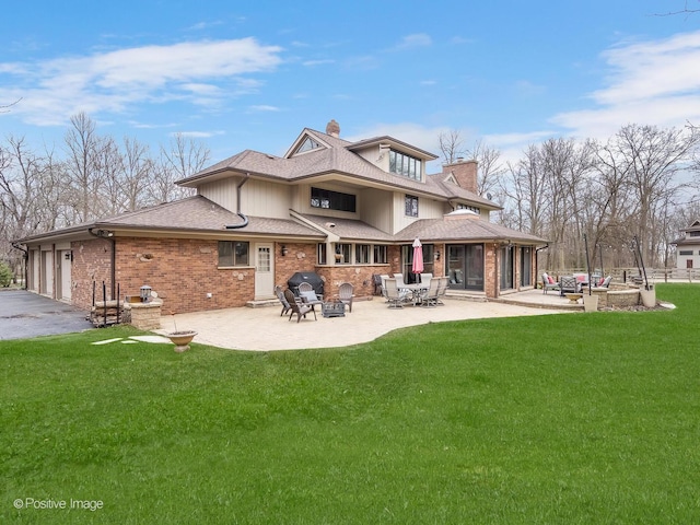 rear view of house featuring roof with shingles, a chimney, a patio area, a yard, and aphalt driveway
