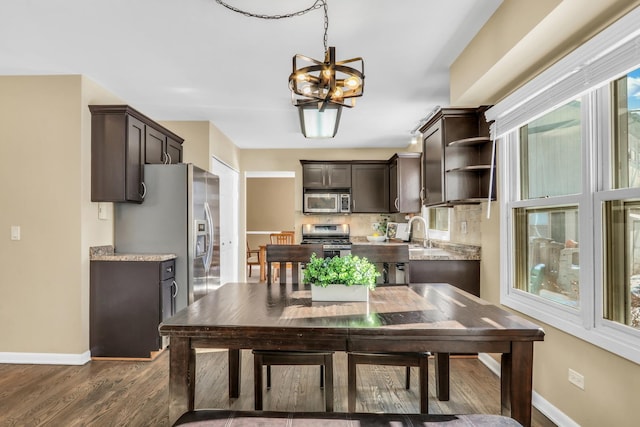 kitchen with dark brown cabinets, appliances with stainless steel finishes, baseboards, and an inviting chandelier