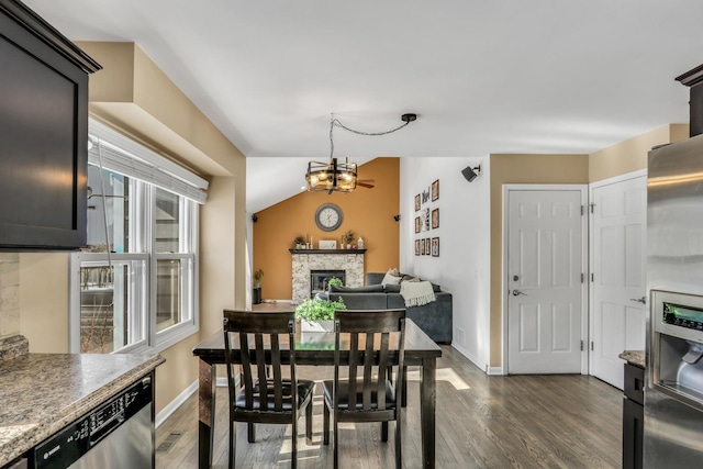 dining room featuring baseboards, a stone fireplace, dark wood-style floors, and an inviting chandelier