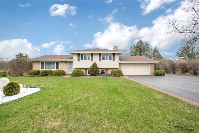 tri-level home featuring an attached garage, a front lawn, a chimney, and aphalt driveway