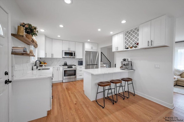 kitchen featuring stainless steel appliances, open shelves, a sink, light wood-type flooring, and a peninsula