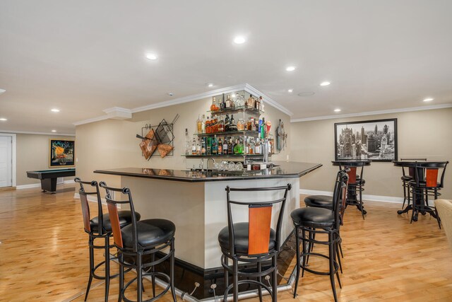 indoor wet bar with recessed lighting, ornamental molding, light wood-style flooring, and baseboards