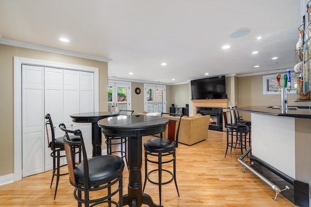 dining space featuring crown molding, a glass covered fireplace, recessed lighting, and light wood finished floors