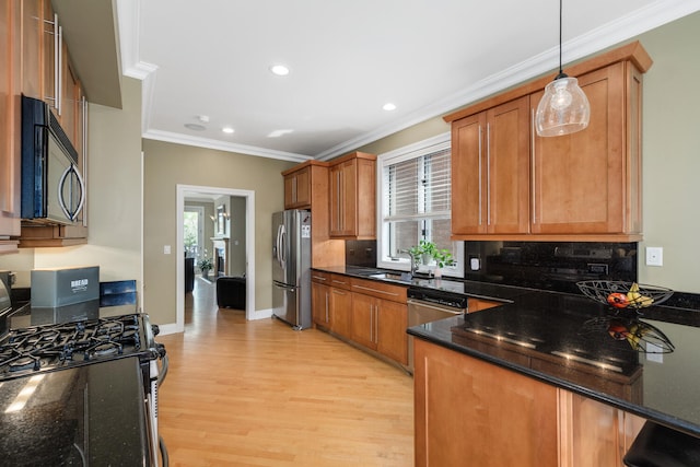 kitchen featuring appliances with stainless steel finishes, a sink, brown cabinets, light wood finished floors, and crown molding