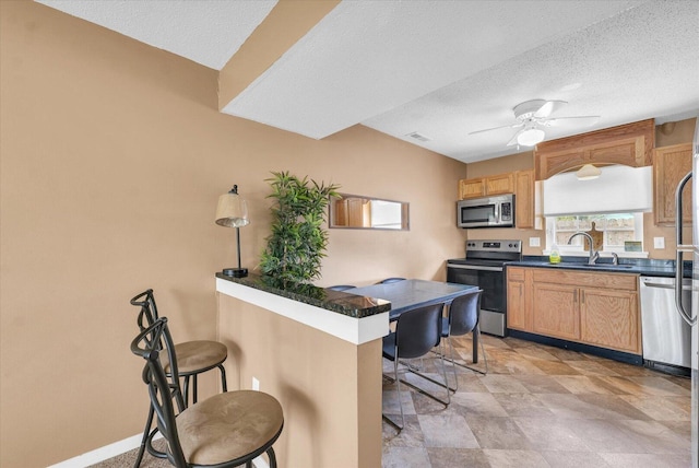 kitchen featuring a sink, stainless steel appliances, a kitchen breakfast bar, dark countertops, and a textured ceiling