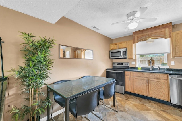 kitchen featuring a textured ceiling, a sink, dark countertops, stainless steel appliances, and a ceiling fan
