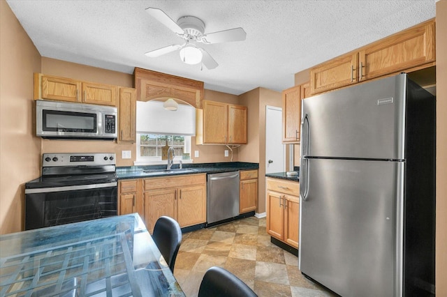 kitchen with a sink, stainless steel appliances, ceiling fan, dark countertops, and a textured ceiling