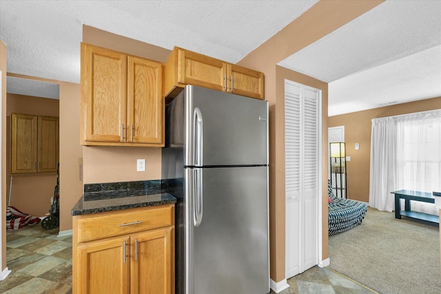 kitchen with dark stone counters, a textured ceiling, freestanding refrigerator, and baseboards
