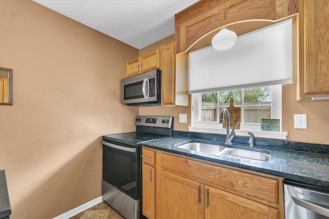 kitchen featuring dark stone countertops, stainless steel appliances, baseboards, and a sink