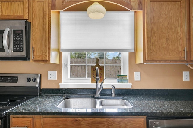 kitchen with dark stone counters, a sink, brown cabinets, and stainless steel appliances