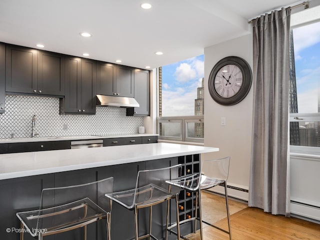 kitchen with recessed lighting, under cabinet range hood, a kitchen bar, and backsplash