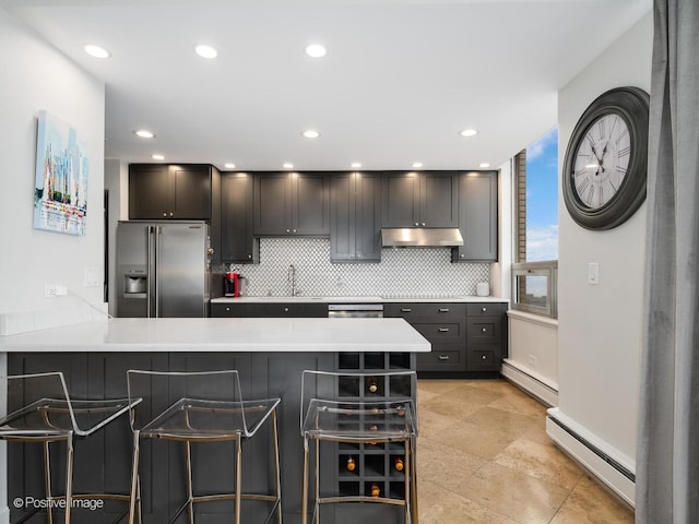 kitchen featuring stainless steel appliances, baseboard heating, light countertops, and a kitchen bar