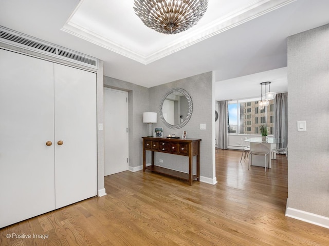 entryway featuring a baseboard radiator, a raised ceiling, light wood-type flooring, and a notable chandelier