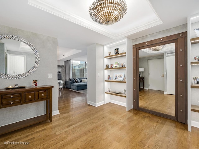 hallway with a chandelier, light wood-style flooring, ornamental molding, and a tray ceiling