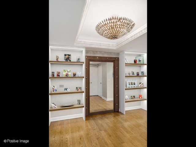 hall with a tray ceiling, light wood-style floors, ornamental molding, and a notable chandelier