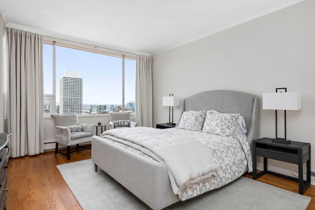 bedroom featuring baseboard heating, a city view, ornamental molding, and wood finished floors