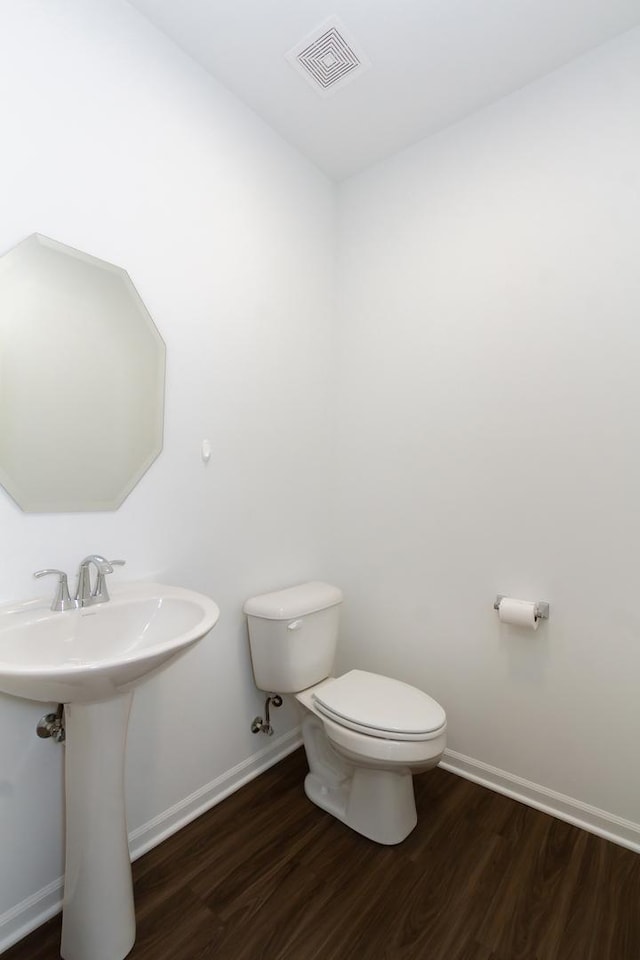half bath with a sink, wood finished floors, baseboards, toilet, and visible vents
