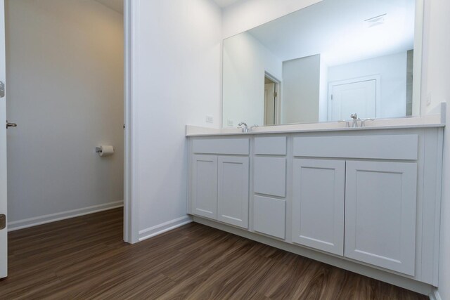 bathroom featuring baseboards, wood finished floors, double vanity, and a sink