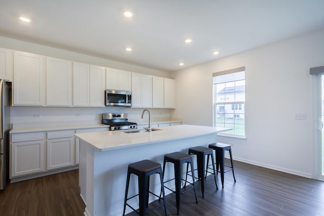 kitchen with a kitchen island with sink, dark wood-style floors, a sink, and appliances with stainless steel finishes