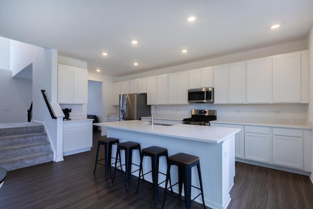 kitchen with a kitchen breakfast bar, a sink, an island with sink, stainless steel appliances, and dark wood-style floors